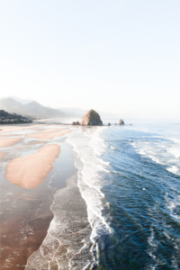 Oregon Coastline with brown sand, blue ocean, and large rocks in distance