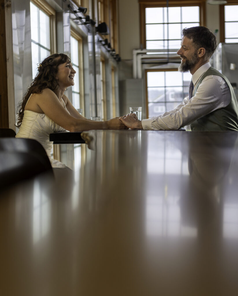 unique perspective of couple holding hands in restaurant, shot with the length of the wood bartop in between couple and camera. 