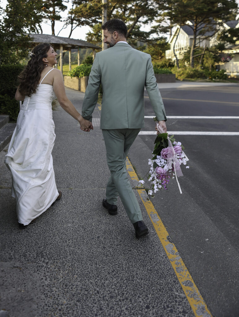 wedding couple walking hand and hand down cannon beach street towards beach