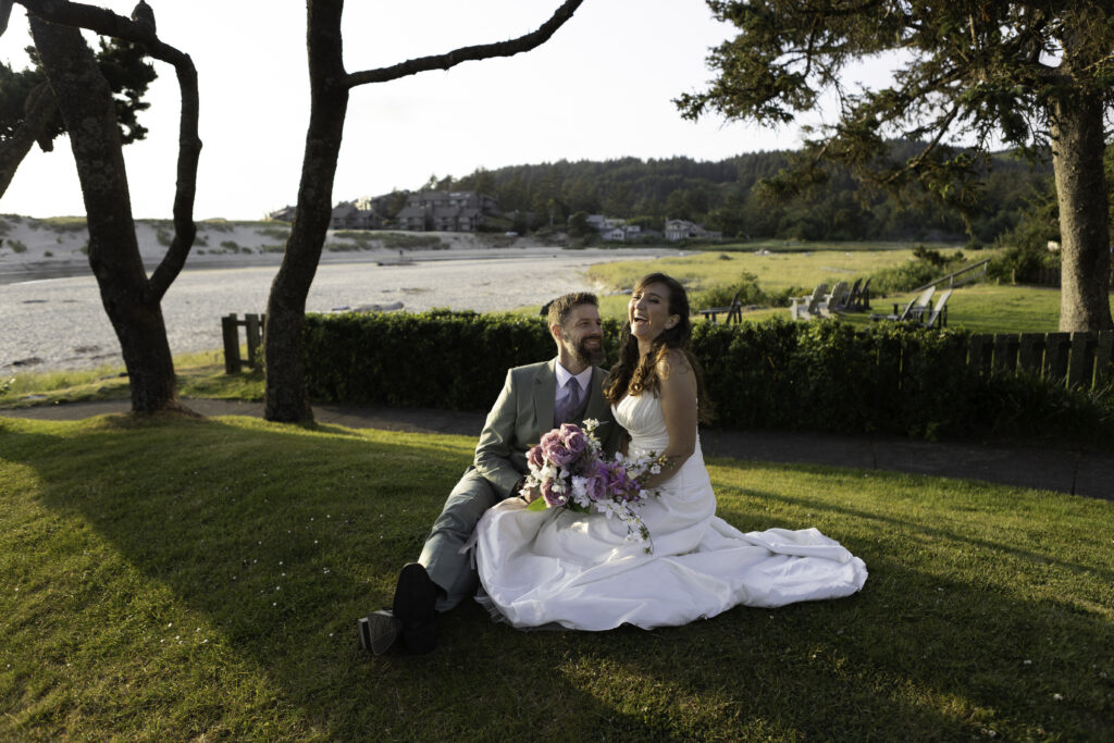 wedding couple sitting on grassy hill near the beach