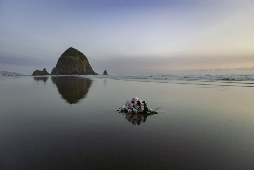 picture of haystack rock with bouquet in forefront laying on the beach. 