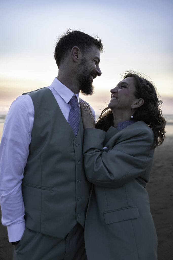 couple standing side by side after their vows. It is cold outside so bride is wearing groom's jacket. they are embracing and staring into each other's eyes