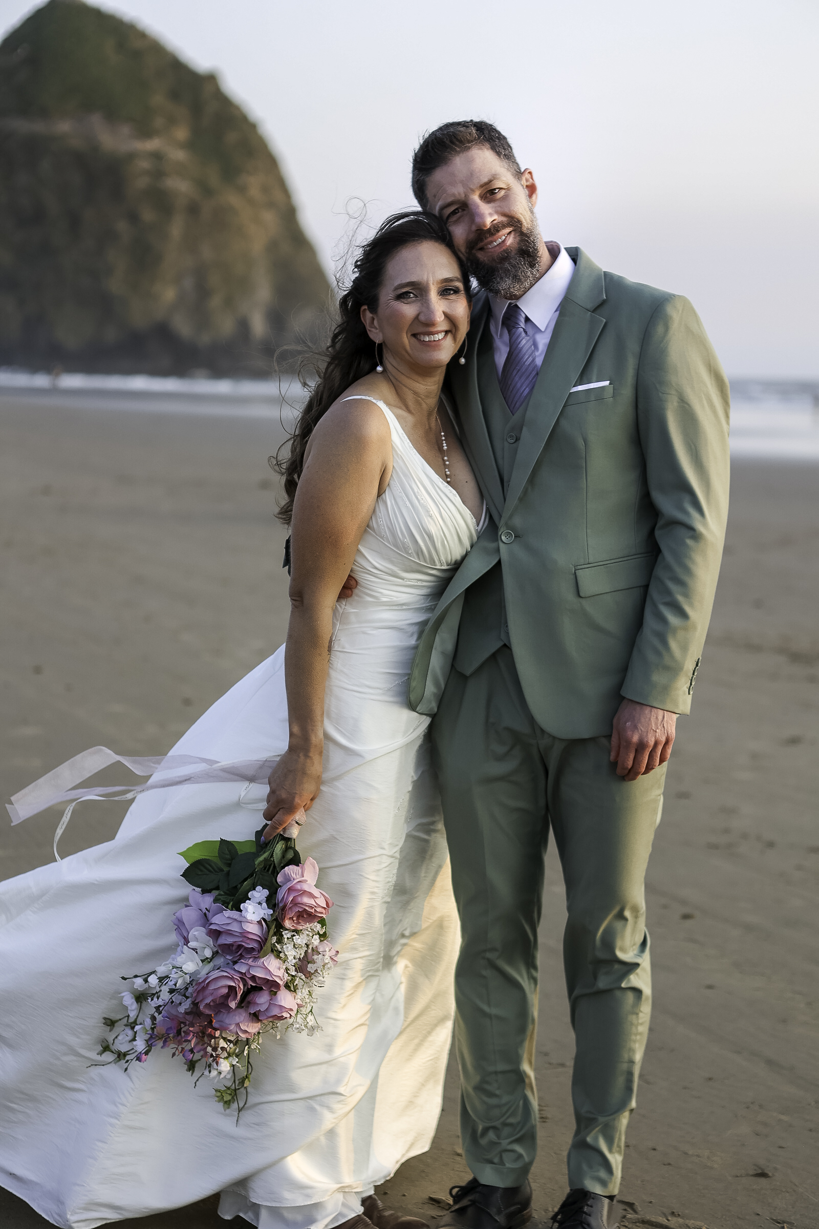 Amber and Jeff stand in front of haystack rock in Cannon Beach Oregon basking in the sunset after saying their vows in a sweet embrace. 