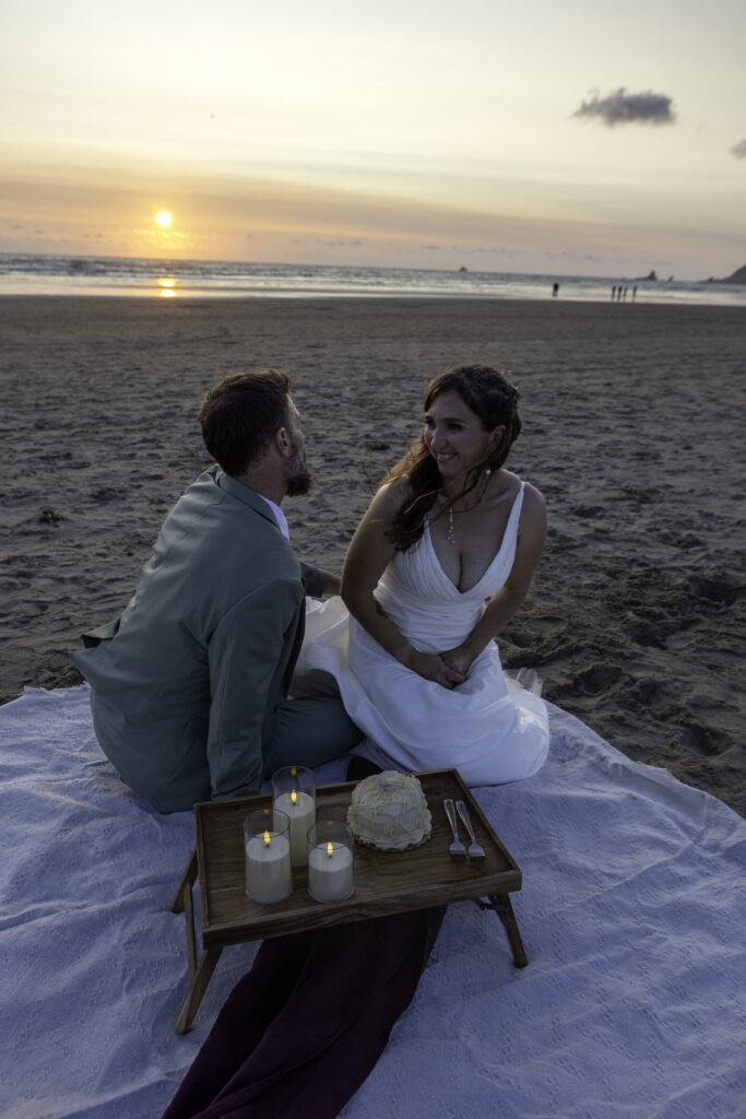 wedding couple has picnic on the beach. they  are looking at each other laughing and talking