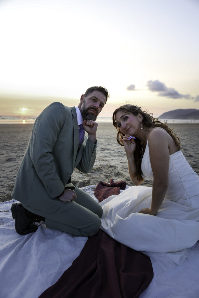 wedding couple striking a silly (serious face) pose after cutting their cake on beach picnic. 