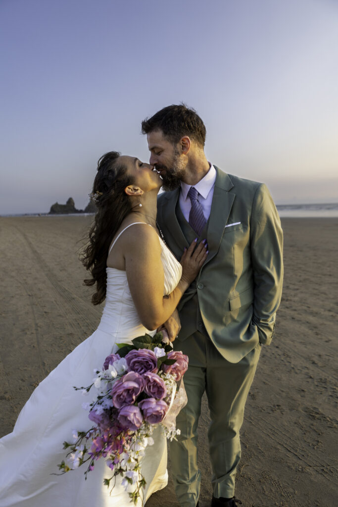 wedding couple stand side by side with bride's hand on his chest as they kiss. 