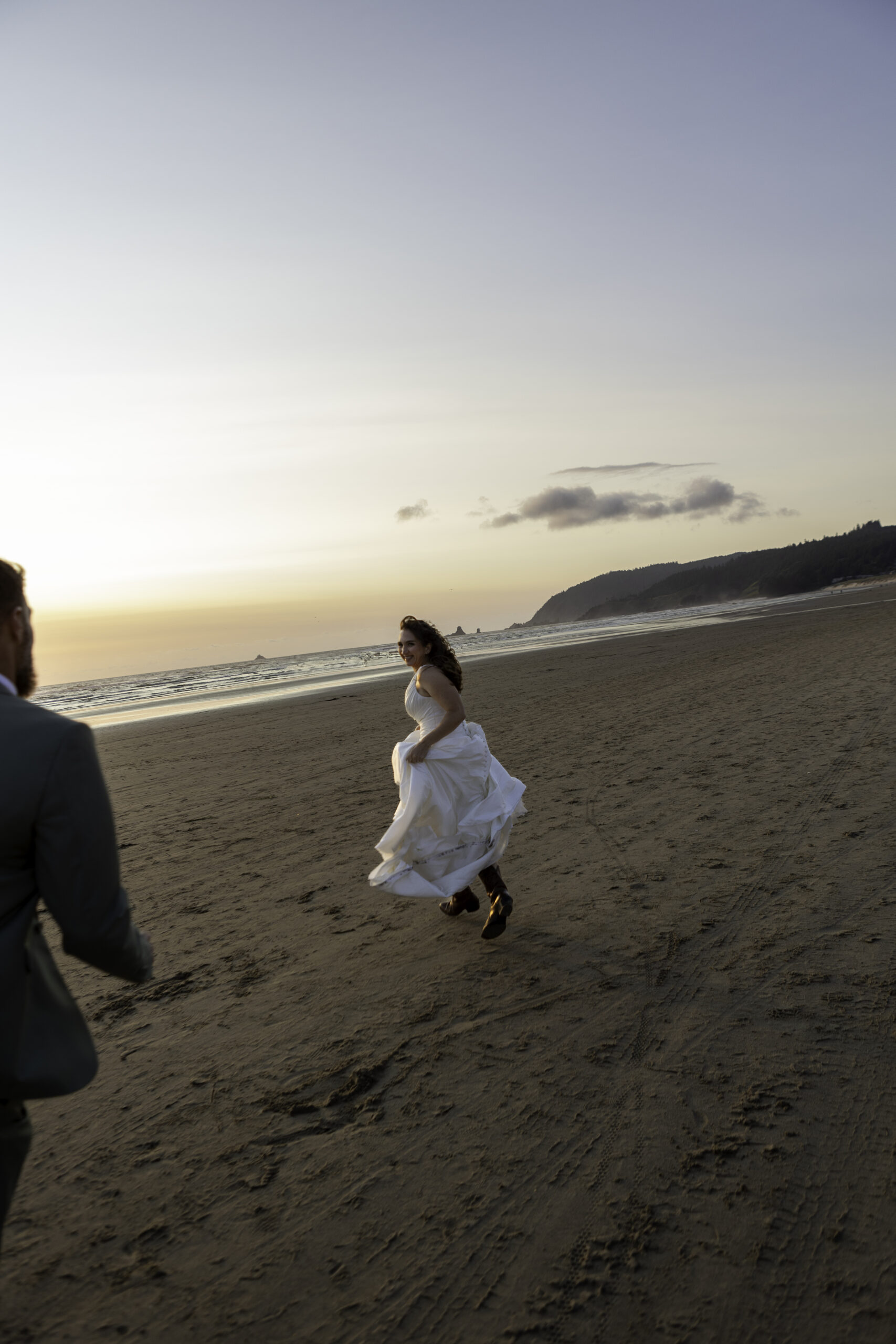 couple play tag in their wedding attire at the beach. 