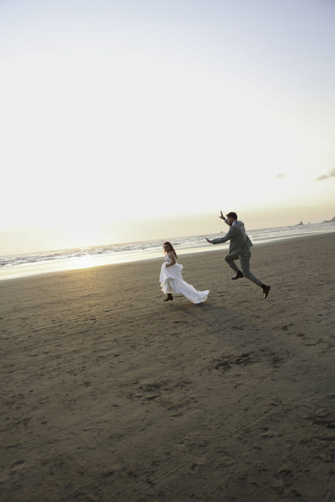 wedding couple play a vigorous game of tag on the beach and he flies through the air playfully