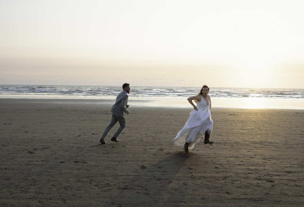 wedding couple play a vigorous game of tag on the beach and she gallops in the air playfully