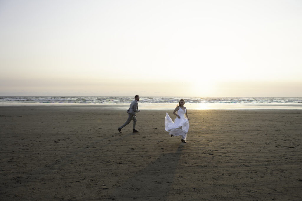 wedding couple play a vigorous game of tag on the beach and she gallops in the air playfully