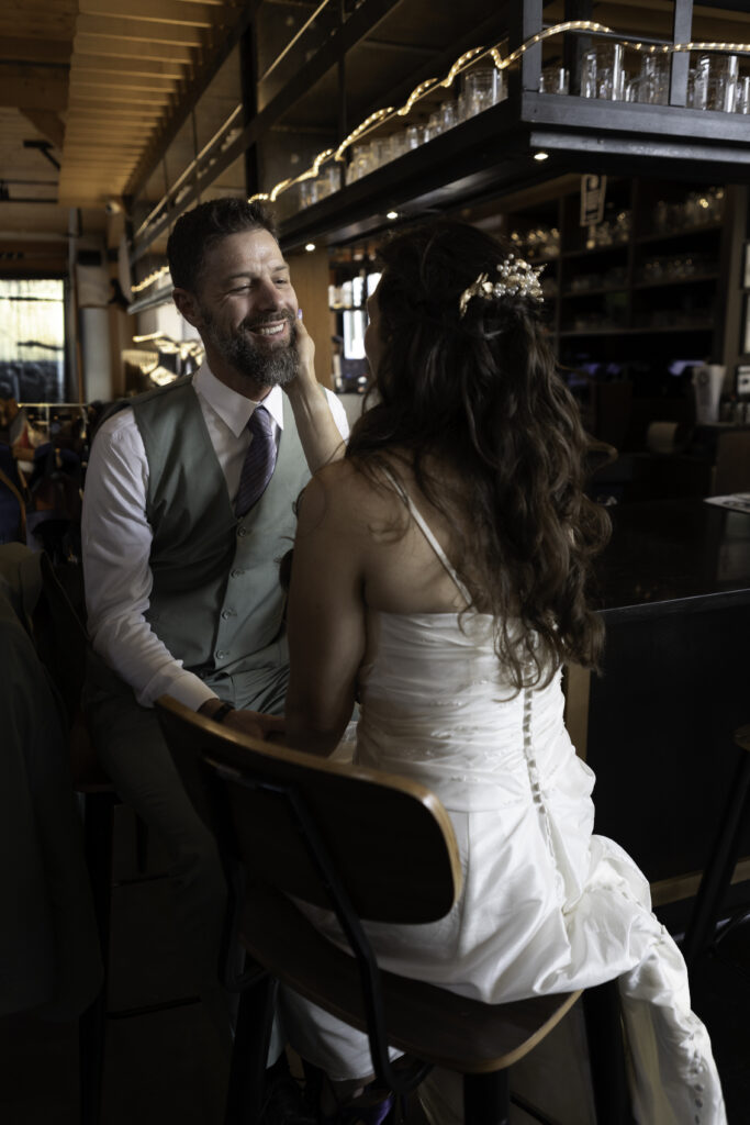sitting at bar, the newlyweds look at each other and hold hands. wife is lovingly embracing his face. 