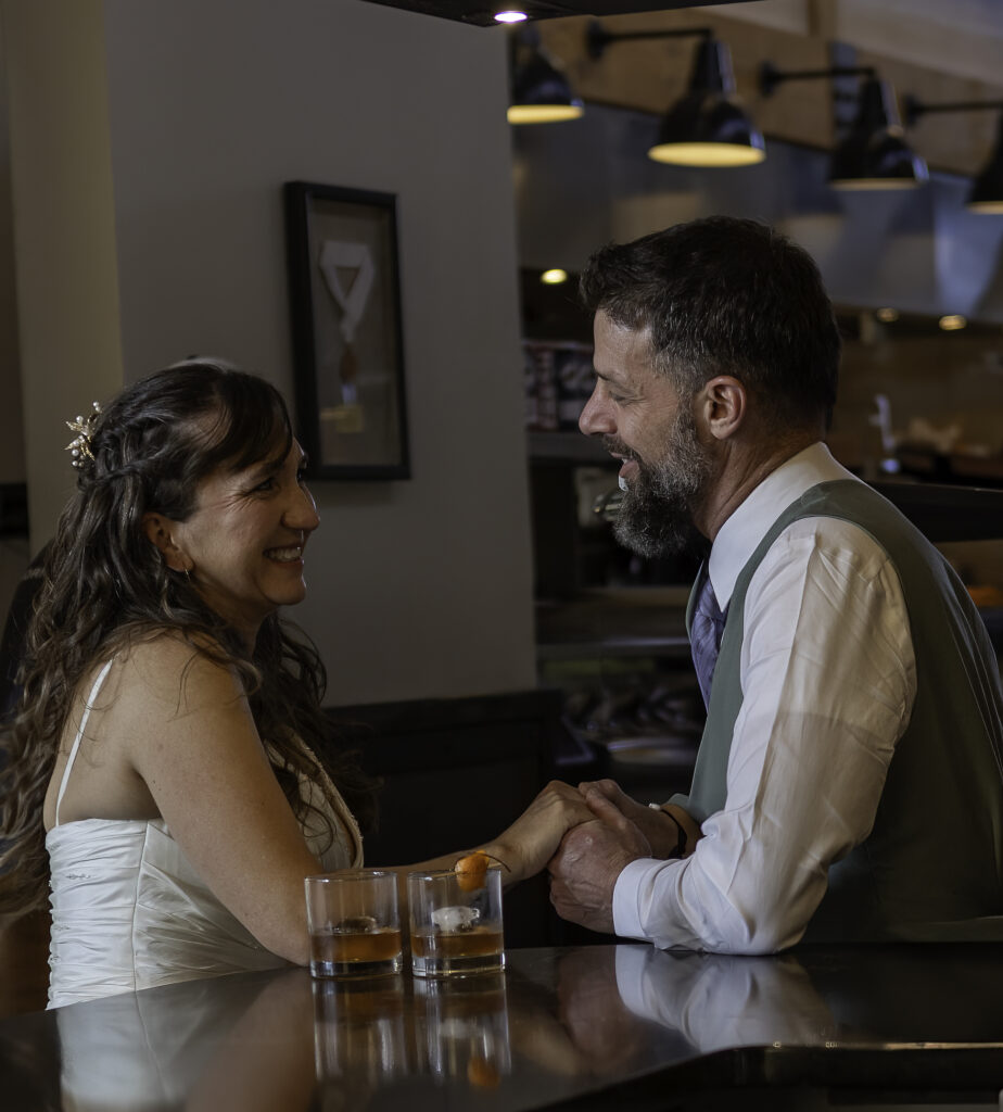 couple sitting at bar looking at each other and holding hands. 