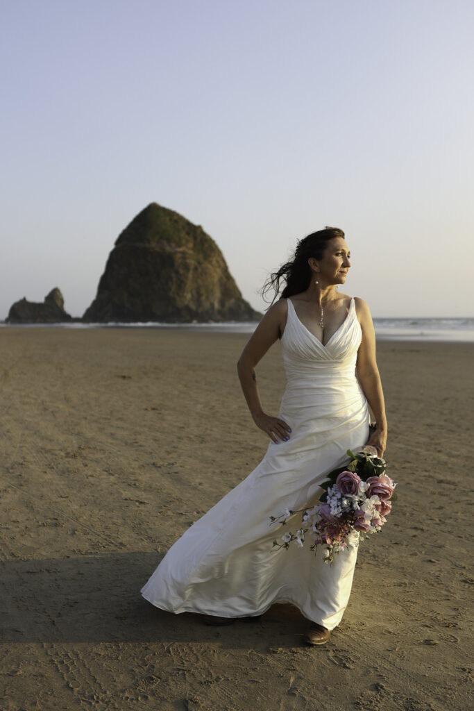bridal portrait in front of haystack rock holding her bouquet. 