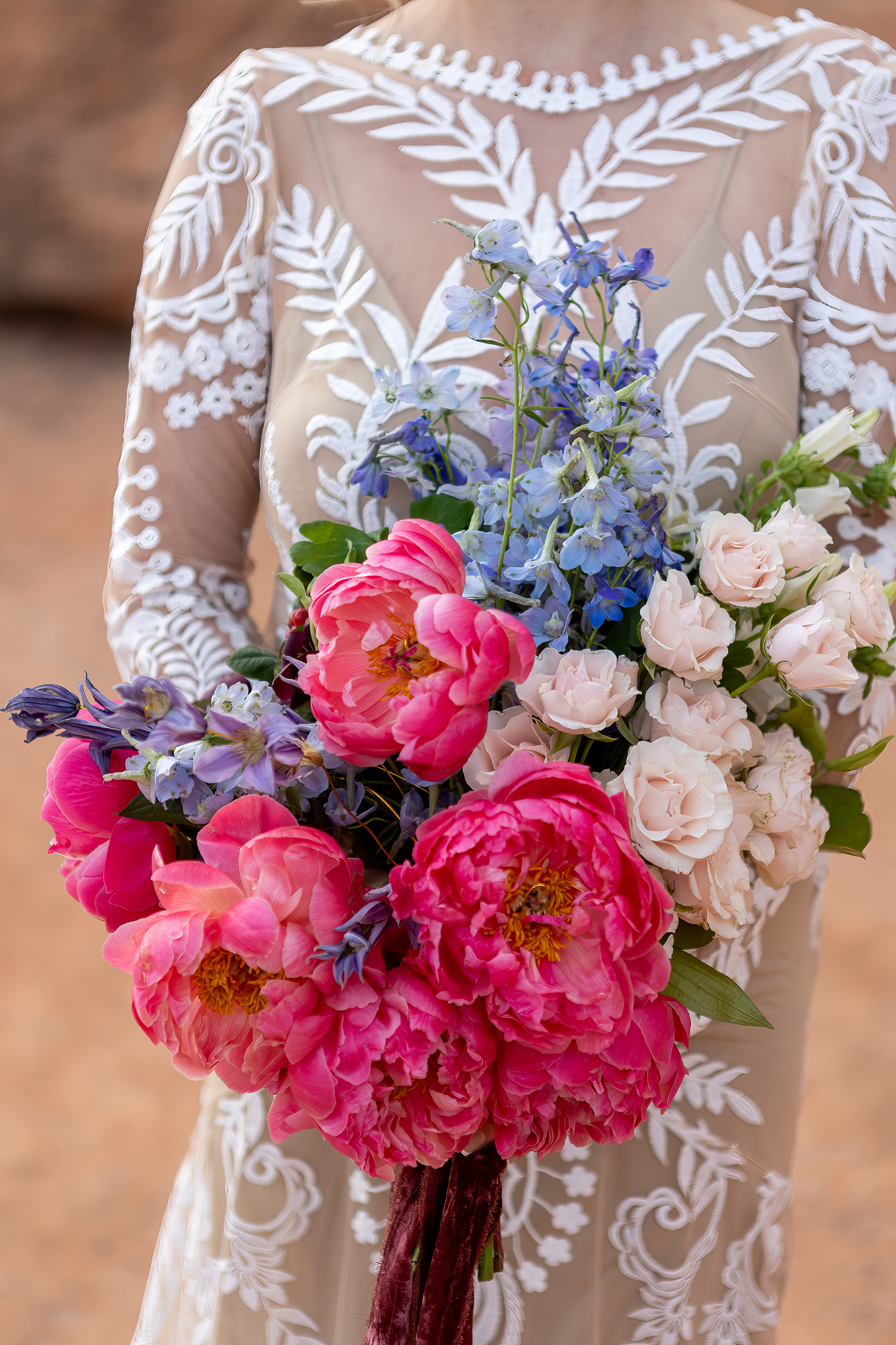 brides bouquet that is mainly bright pink peonies with some blue and pale pink flowers as supplements