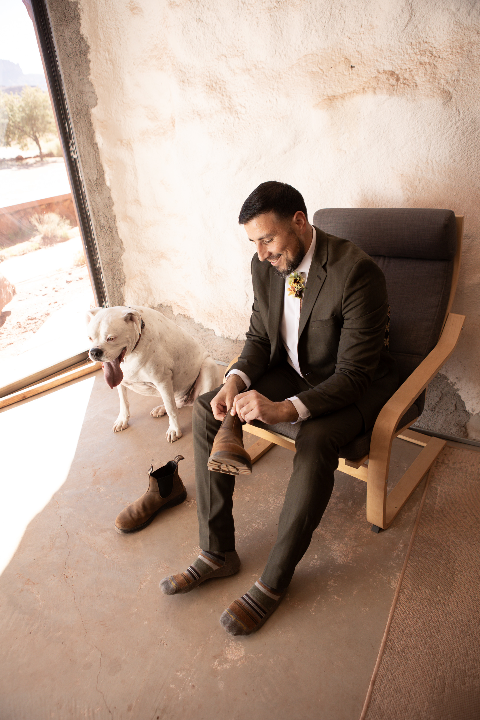 Hugo sitting on chair putting on shoes, next to pongo their dog