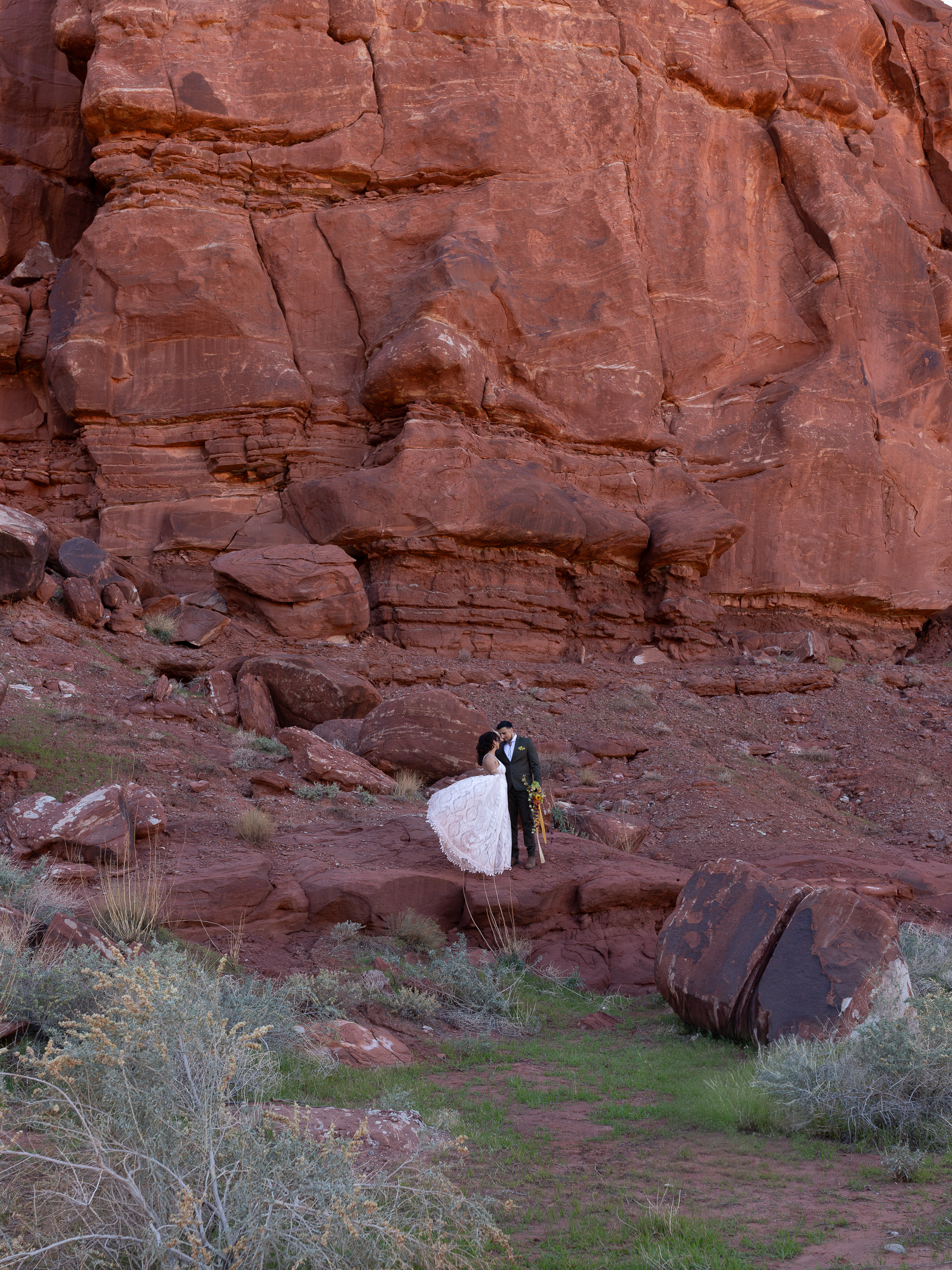 hugo and laura stand on a rock to kiss with towering red rocks behind them