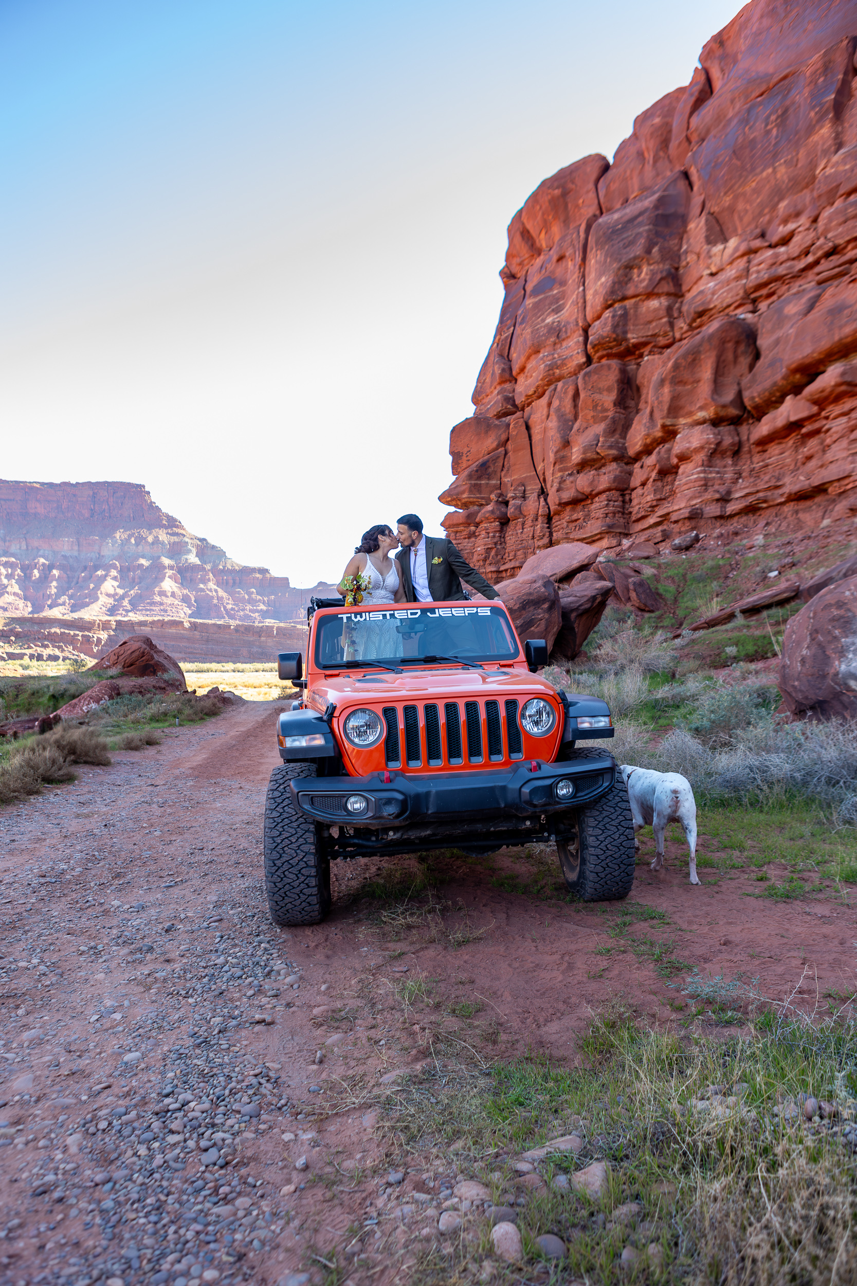 Laura and Hugo stand on front seats of jeep and have heads outside of top that is off of jeep. 
