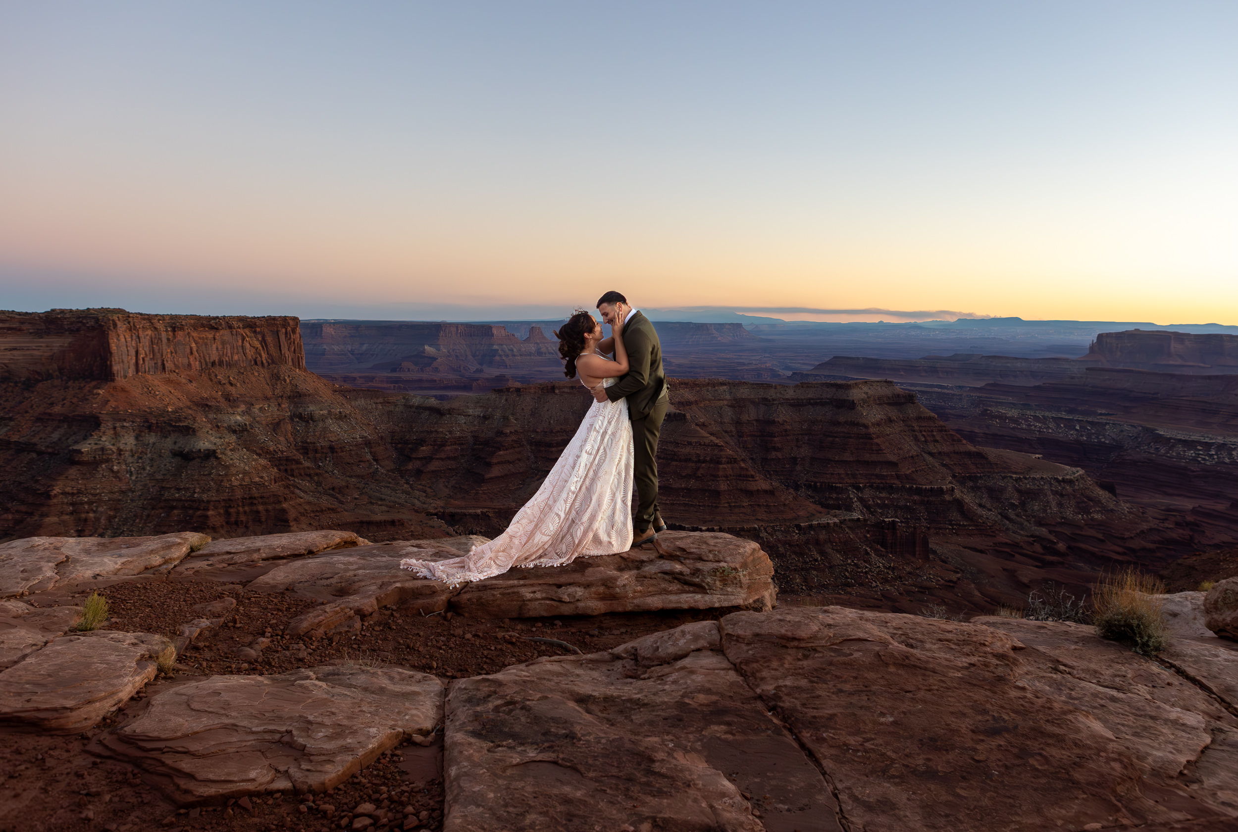couple embacing and looking at each other lovingly on the edge of a cliff overlooking the red rocks of Moab. 