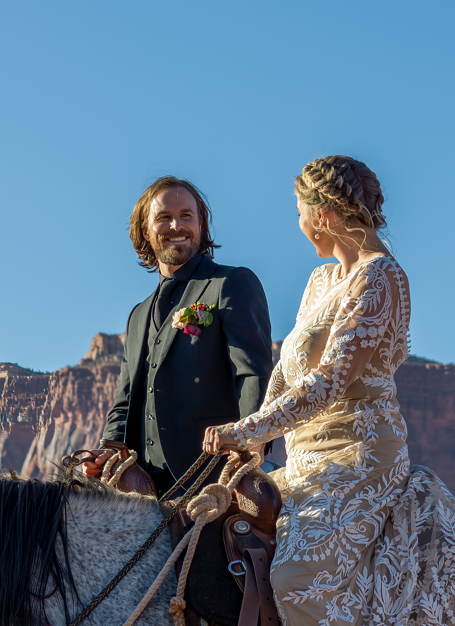 couple looking at each other in wedding attire on horses.