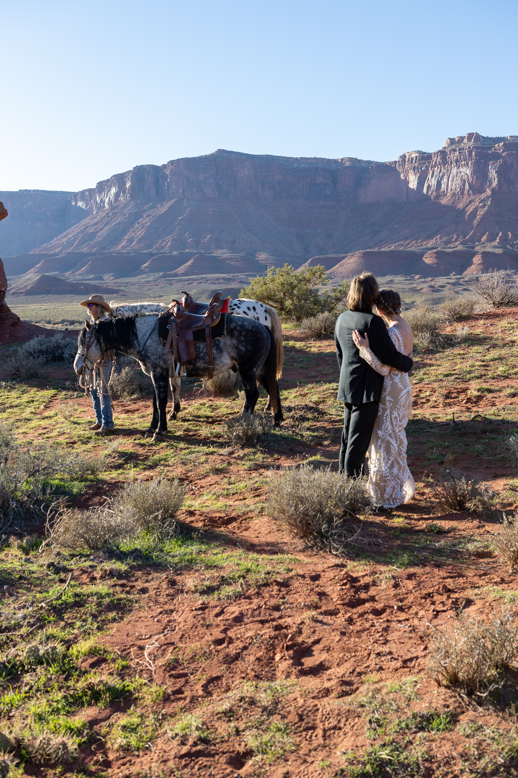 couple embracing and enjoying the view with horses and ranch hand in distance