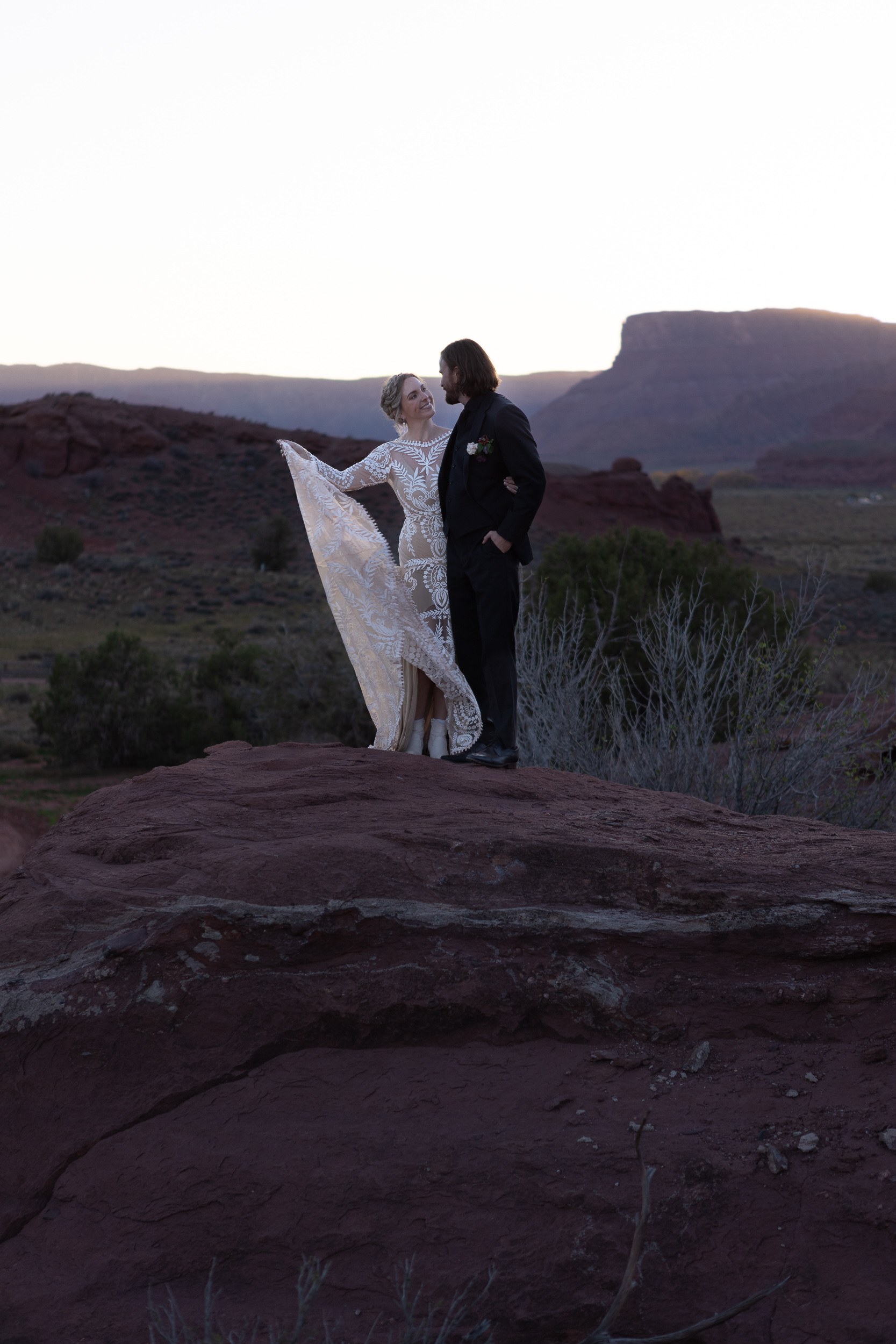 couple pose on rock with sun setting behind mountains in moab closer up