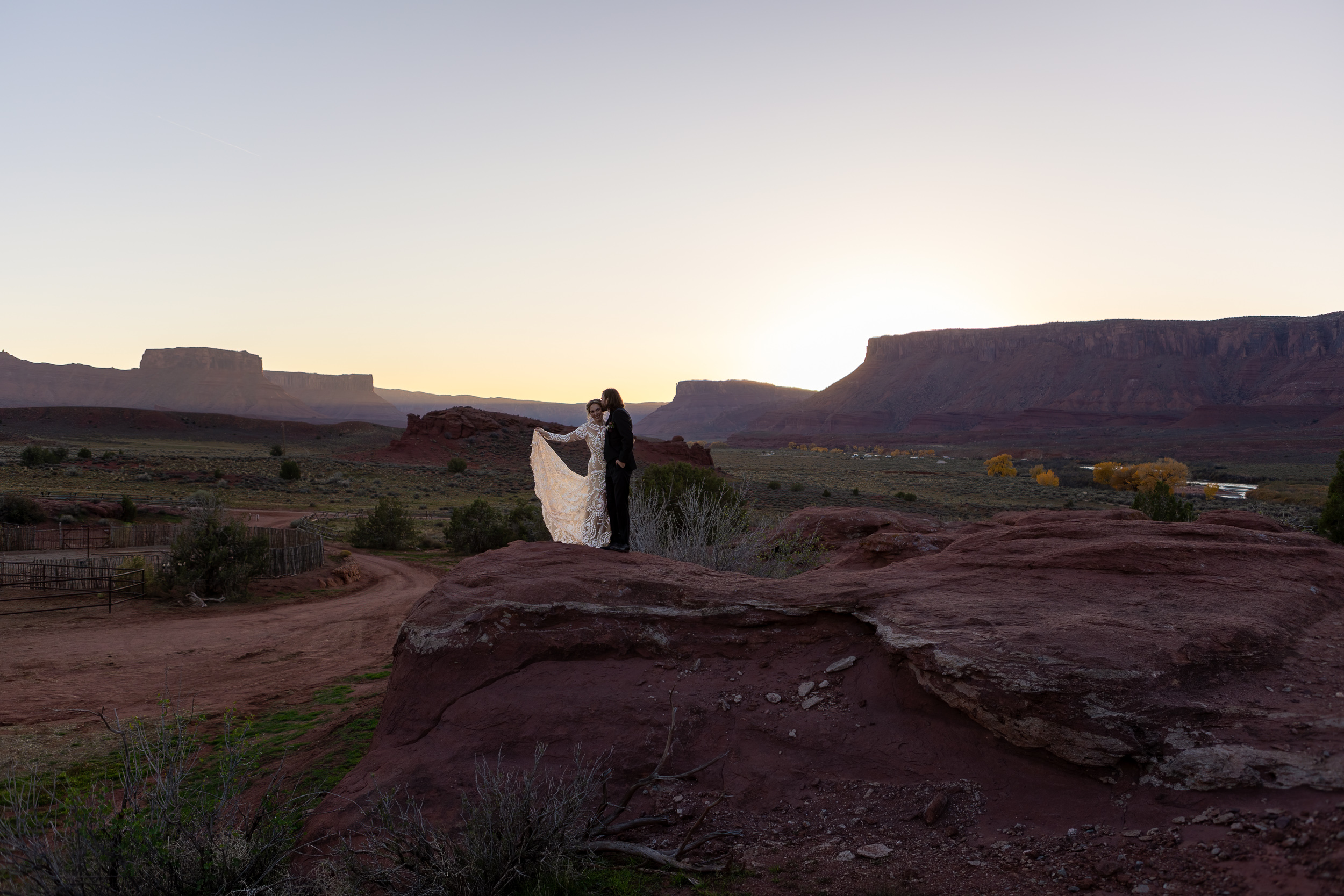 couple pose on rock with sun setting behind mountains in moab