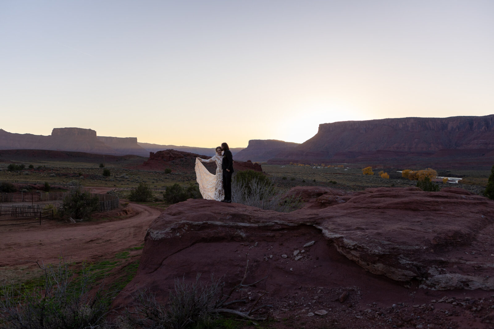 stunning image of couple bathed in sunset glow. Standing on rock on ranch with mountains and river in background