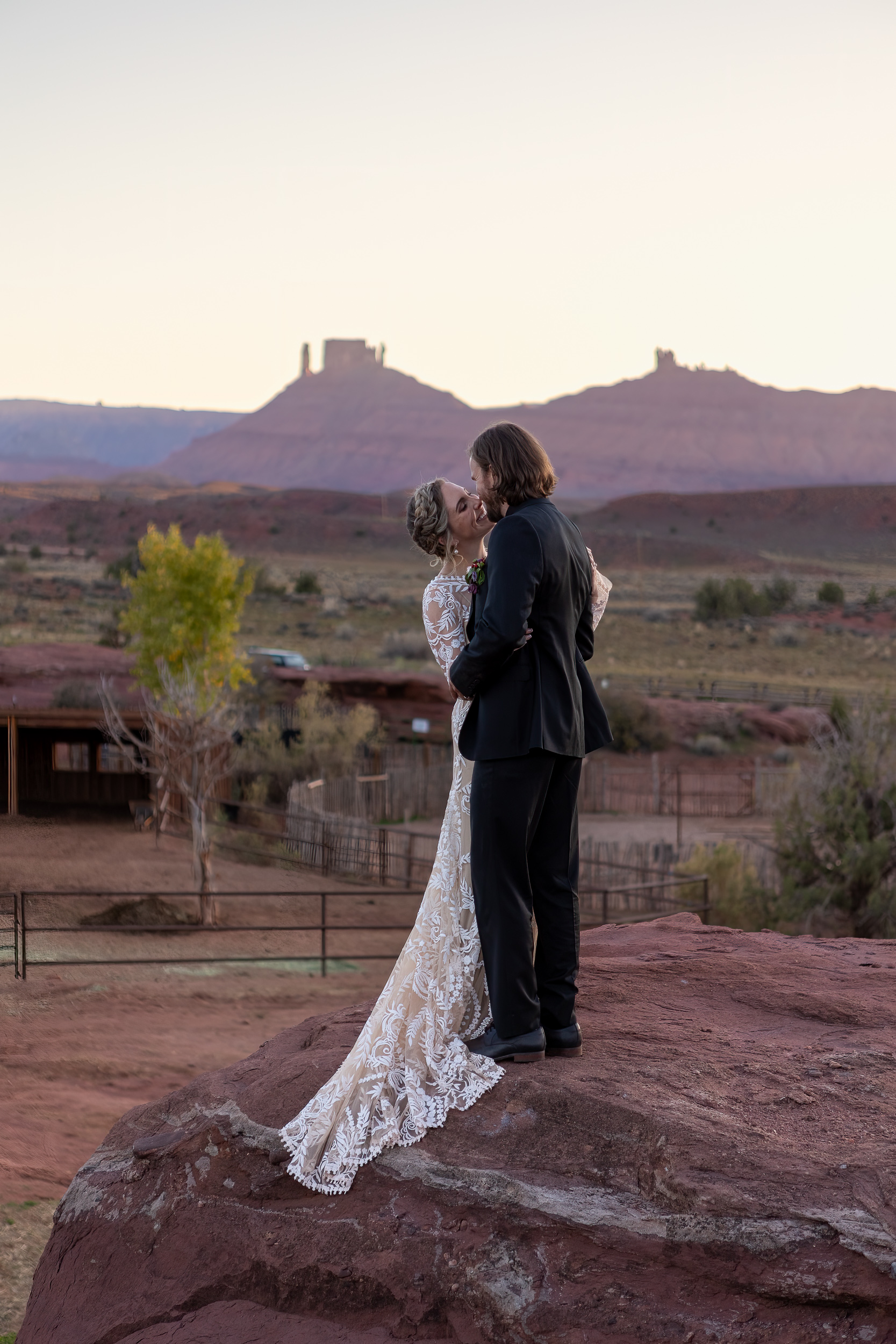couple standing on rock kissing in sunset glow with ranch in background
