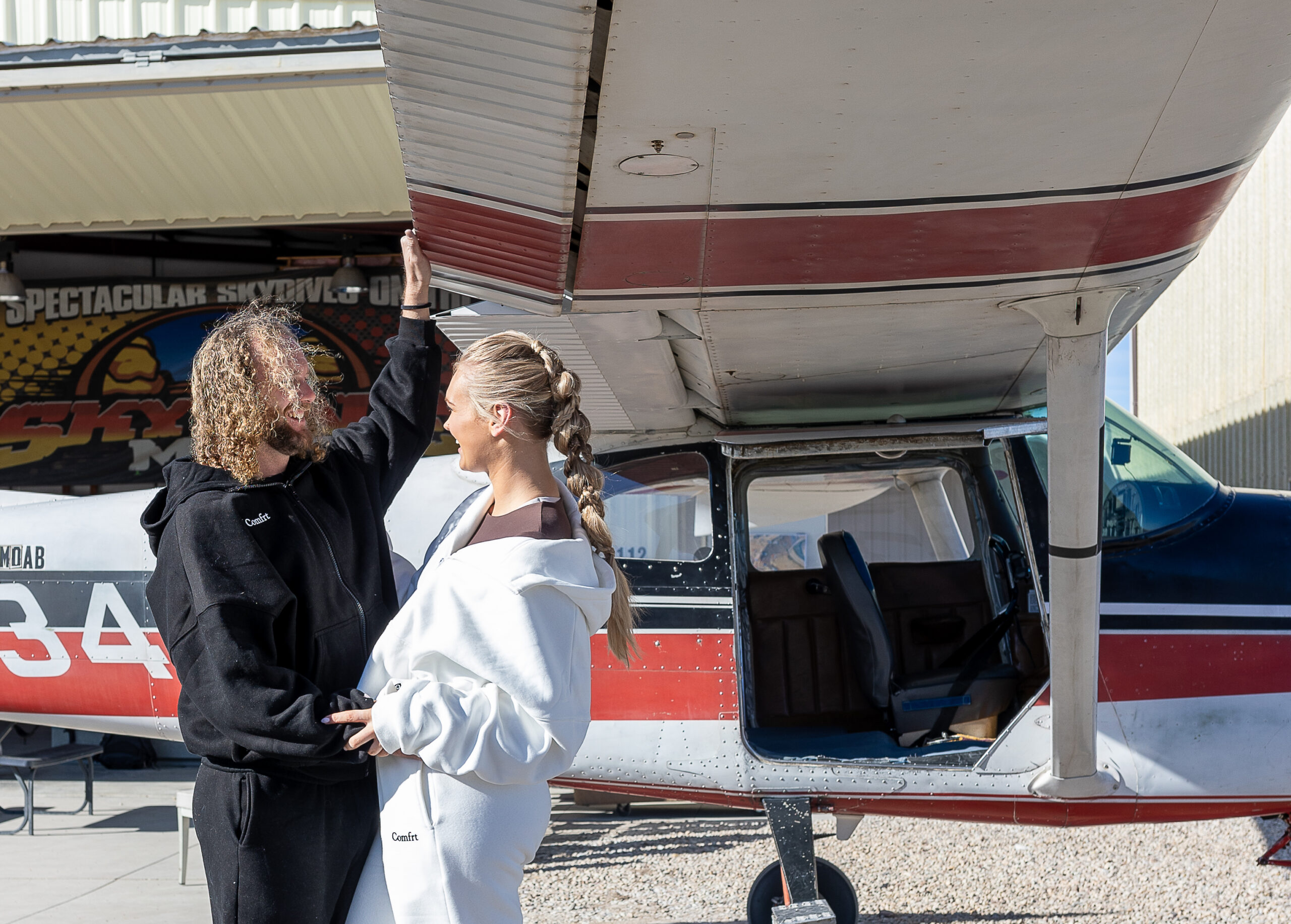 couple taking portraits near a small plane before their skydiving elopement in Moab