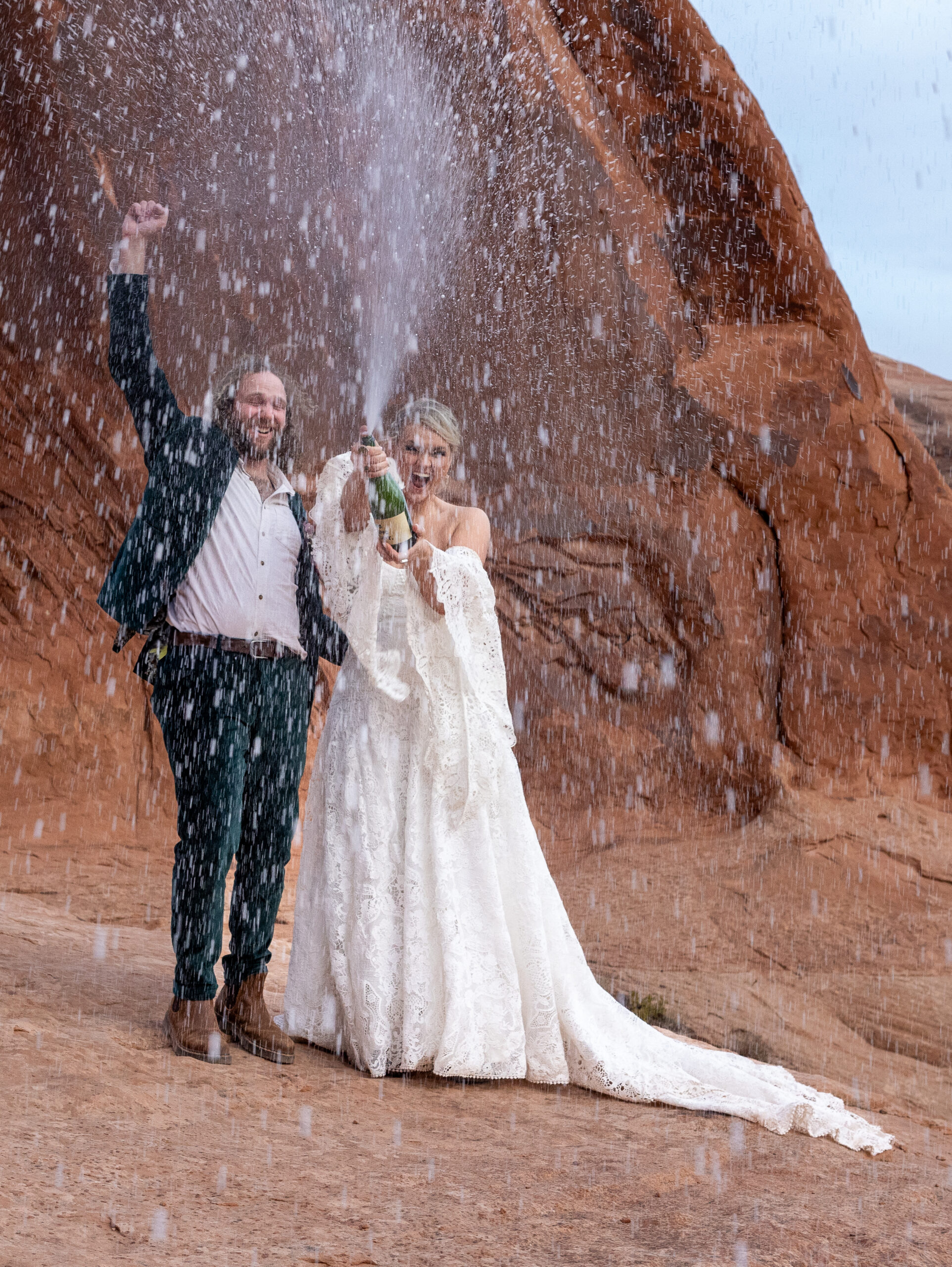 Couple celebrating their elopement by spraying champagne on a red rock overlook in Moab, Utah