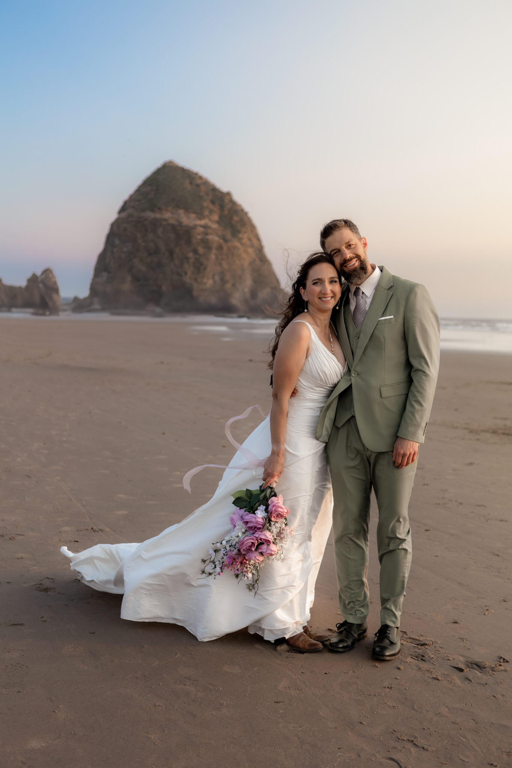 couple embracing at golden hour with haystack rock in background. 