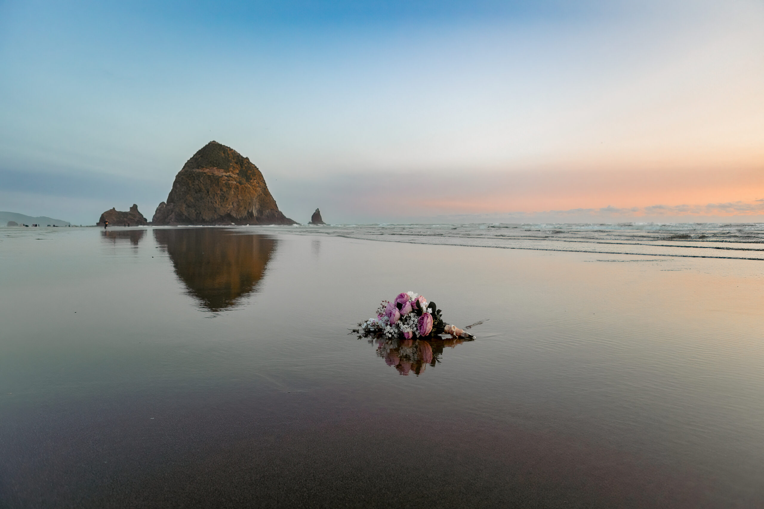 iconic haystack rock at cannon beach oregon with brides floral bouquet in view in front. 