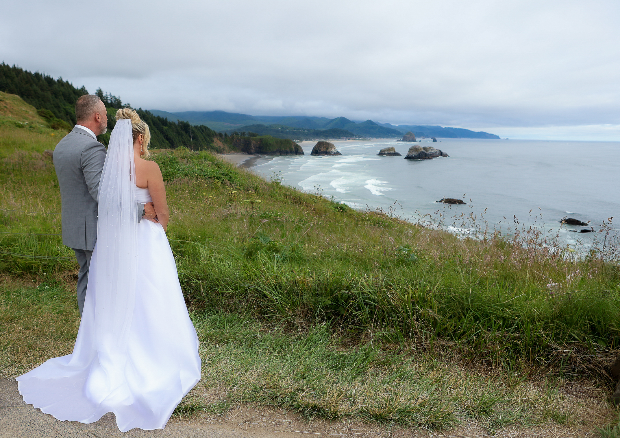 bride and groom embracing, enjoying the view from on top of the cliffs overlooking cannon beach 
