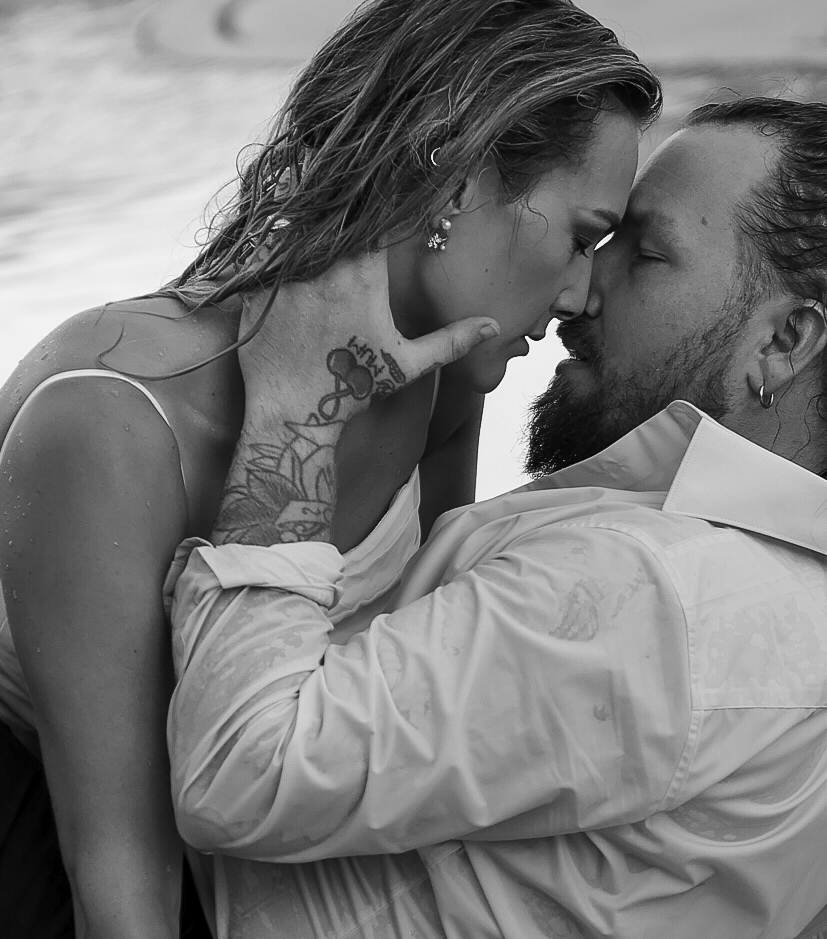 couple wet from surf, go in for a kiss in wedding attire. 