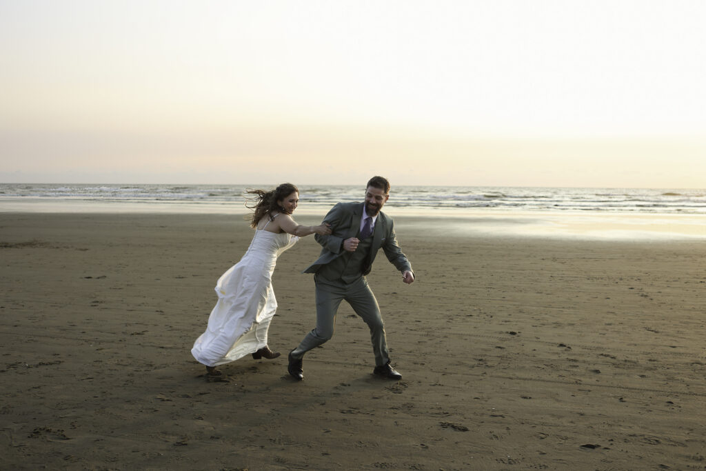 bridal couple spontaneously play a game of tag on the beach during their downtime during an elopement at Cannon Beach oregon